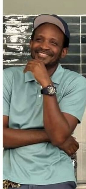 A man in a blue shirt smiles and rests his chin on his hand.