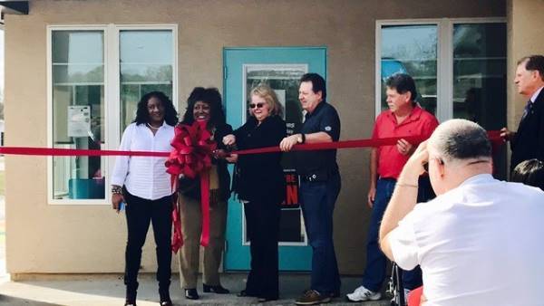 A group of men and women cutting a large ribbon. 